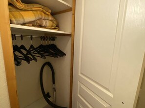 Ein Schrank mit Kleidern und einem Staubsauger.