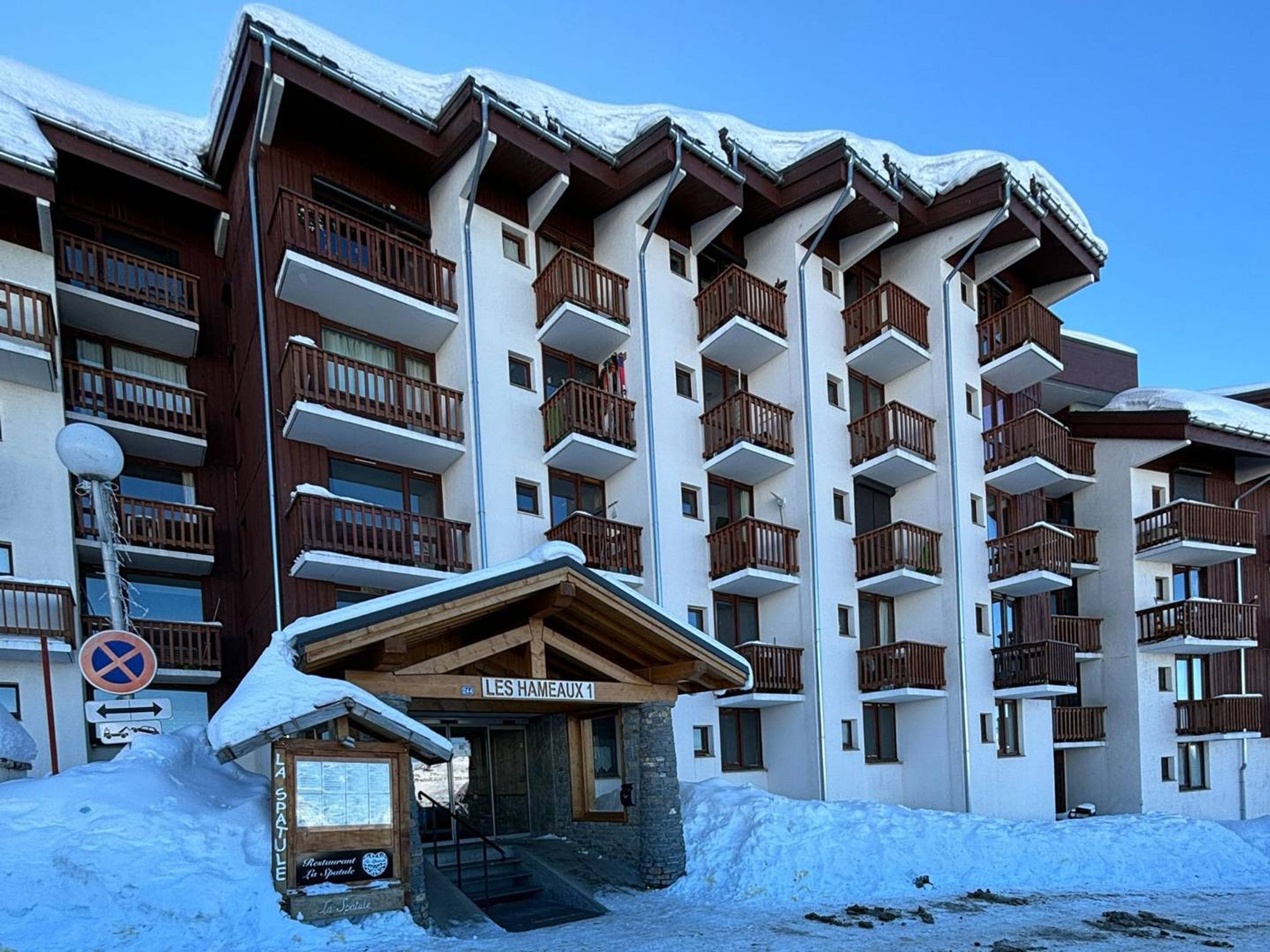 A multi-story hotel with balconies, a sign reading "LES HAMEAUX 1", and a small entrance building with a sign for "La Spatule".