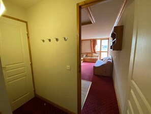A hallway leading to a bedroom with a bed, a window with curtains, and a door with a light switch. - Charming studio, balcony mountain view - 4 guests (Plagne Villages)