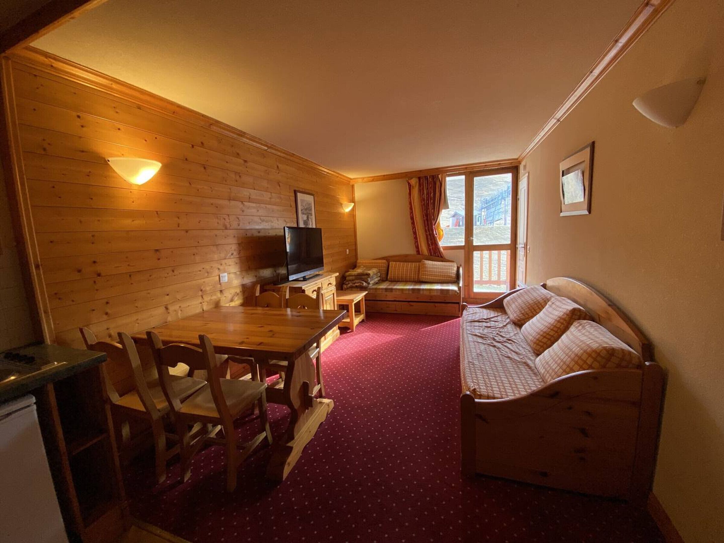 A cozy room with a wooden wall, a television, a sofa, and a dining table with chairs.