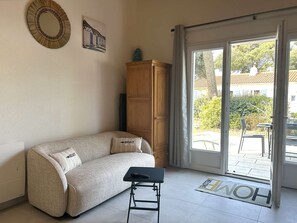 A living room with a sofa, a small table, a wooden cabinet, and a sliding glass door leading to an outdoor area. - Renovated house close to the beach - 3 guests (Bretignolles-sur-Mer)
