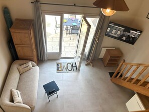 A living room with a sofa, a small table, a wooden cabinet, a staircase, and a door leading outside. - Renovated house close to the beach - 3 guests (Bretignolles-sur-Mer)