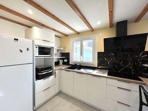 A compact kitchen with white cabinetry, a built-in oven, a microwave, a black stove, and a window with a view of the outside. - Renovated house close to the beach - 3 guests (Bretignolles-sur-Mer)