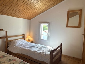 A bedroom with a wooden ceiling, a single bed with white bedding, a nightstand with a lamp, and a window with a view of greenery. - Renovated house close to the beach - 3 guests (Bretignolles-sur-Mer)