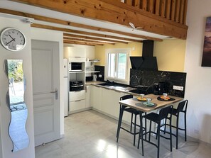 A modern kitchen with a built-in oven, microwave, and a black stove. There is a dining area with a table and chairs. - Renovated house close to the beach - 3 guests (Bretignolles-sur-Mer)