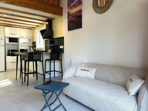 A compact living space with a kitchenette, a sofa with a pillow, and a small table. - Renovated house close to the beach - 3 guests (Bretignolles-sur-Mer)