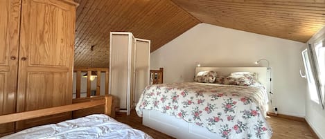 Une chambre avec un plafond en pente, une armoire en bois, un lit avec une literie à motifs floraux et une table de chevet.