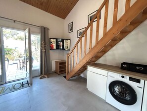Un área de lavandería con lavadora, una escalera de madera y un televisor montado en la pared.