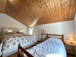 Un dormitorio con dos camas, techo de madera, paredes blancas y una mesita de noche con una lámpara.