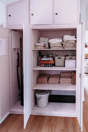Ein weißer Kleiderschrank mit mehreren Einlegeböden, auf denen gefaltete Handtücher und Kartons sowie ein Eimer liegen.