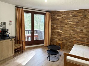 Une pièce dotée d’un plancher en bois, d’une table à manger, d’une petite table ronde, d’un canapé, d’une machine à café et offrant une vue sur un balcon avec une balustrade en bois.