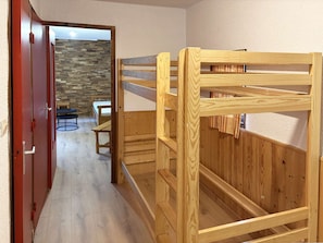 A wooden bunk bed with a stone wall and a dining area in the background. - Spacious apartment at the foot of the slopes - 6 guests (Les Orres)