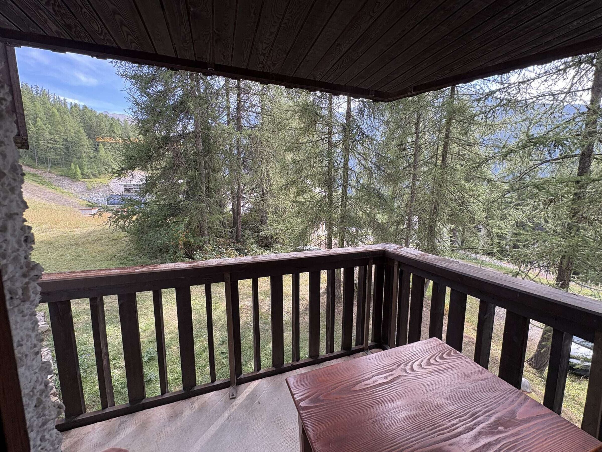 A wooden deck with a bench, overlooking a forested area with a view of a distant building.