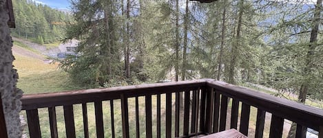 A wooden deck with a bench, overlooking a forested area with a view of a distant building.