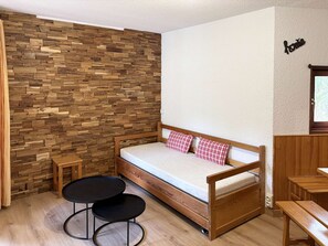 A single bed with a wooden frame and a mattress, two black round tables, a wooden wall with a herringbone pattern, and a small wooden stool. - Spacious apartment at the foot of the slopes - 6 guests (Les Orres)