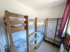 Ein Schlafraum mit einem Etagenbett aus Holz, einem Metallschrank und einem kleinen Fenster mit Vorhang.