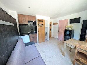 A compact living space with a kitchenette, a sofa, a dining table, and a TV mounted on the wall. - Renovated studio facing slopes - 3 guests (Montgenèvre)