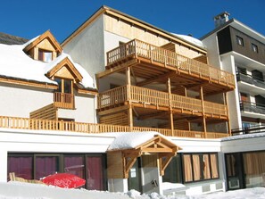 Ein mehrstöckiges Gebäude mit hölzernen Balkonen und einer Skipiste im Vordergrund.