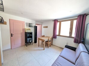 A compact living space with a dining table, a sofa, a TV, and a kitchenette area.
