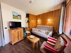 A cozy living room with a wooden cabinet, a television, a sofa, and a chair. - Duplex apartment, balcony with pine view - 6 guests (La Plagne Tarentaise)