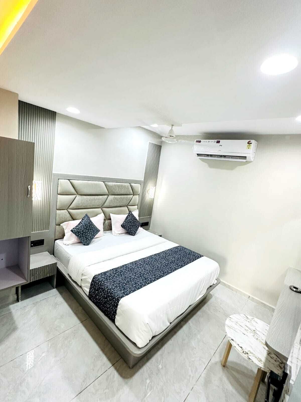 A modern bedroom with a large bed, a bedside table, an air conditioning unit, and a lamp.