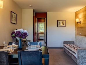 A dining area with a table set for four, a vase with flowers, and a sofa in the background. - Apartment with slope view - 4 guests (Belle Plagne)