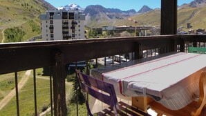 Ein Balkon mit Tisch und Stühlen mit Blick auf eine gebirgige Landschaft mit Gebäuden und einer Straße.