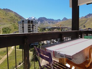 Ein Balkon mit Tisch und Stühlen mit Blick auf eine gebirgige Landschaft mit Gebäuden und einer Straße.