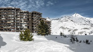 Ein mehrstöckiges Hotel mit Balkonen, im Hintergrund ein verschneiter Berg und ein klarer Himmel.