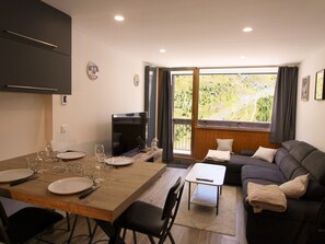 A modern living space with a dining area, a sofa, and a large window offering a view of a green landscape. - Cozy apartment - 4 guests (Tignes)
