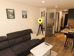 A modern living room with a dark sofa, a small white table, and a floor lamp. - Cozy apartment - 4 guests (Tignes)