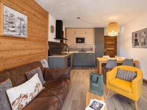 A cozy living room with a brown sofa, a yellow armchair, and a dining area with a table and chairs. - Pleasant apartment, mountain view - 4 guests (Le Monêtier-les-Bains)