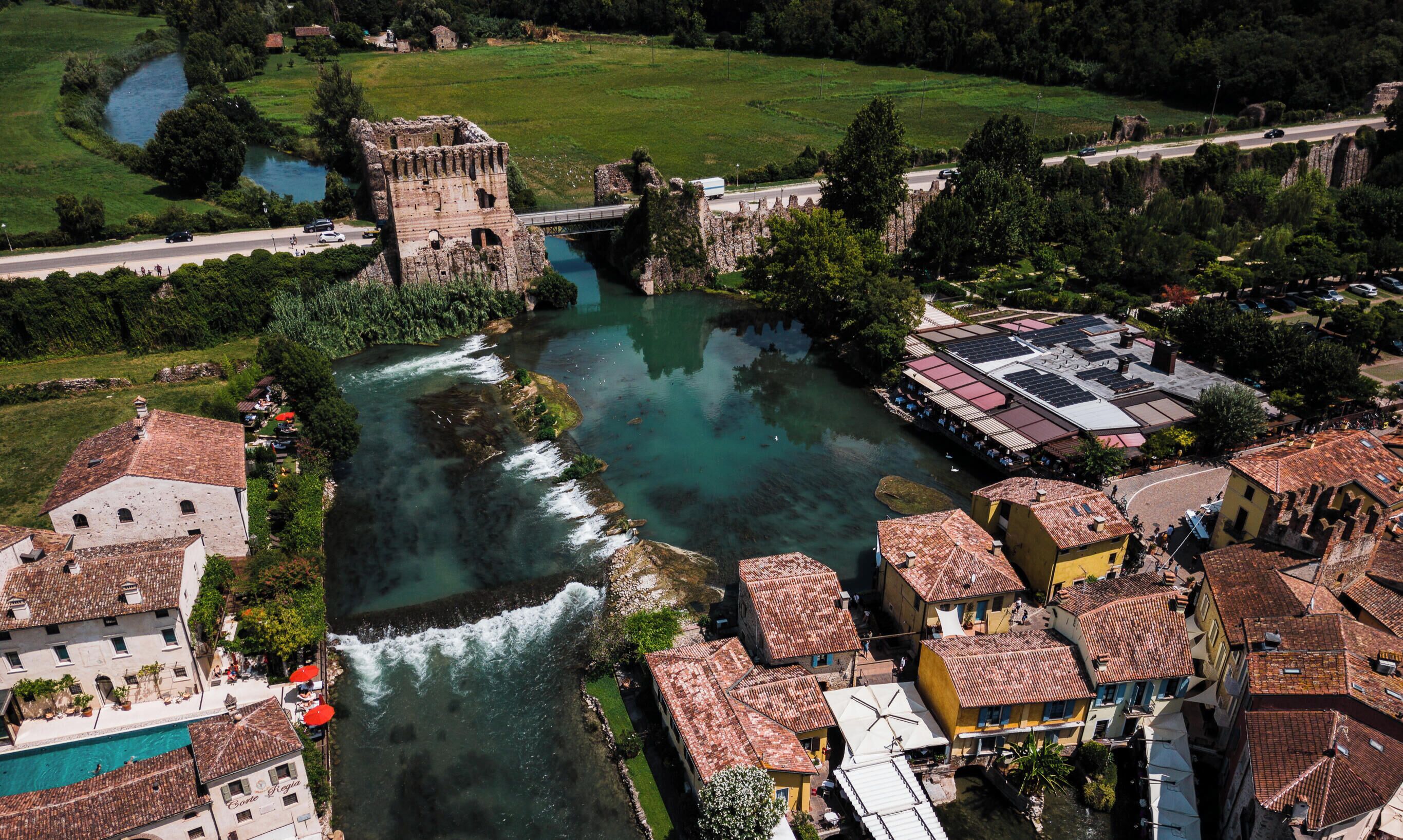 A riverside town with historic buildings, a bridge, and a swimming area.