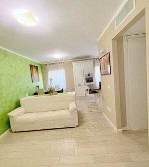 Una sala de estar con sofá, una zona de comedor con mesa y sillas, y una cocina con alacenas y electrodomésticos.