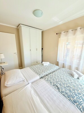 Una habitación con dos camas, un armario, una lámpara y una ventana con cortinas.