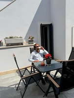 Una persona sentada en una mesa al aire libre con una planta en maceta y un vaso de bebida.