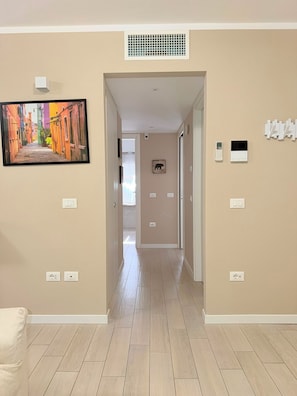 A hallway with beige walls, a tiled floor, and a painting of a colorful street scene. There are light switches and a thermostat on the walls. - Casa Magenta Apartment 3 (Valeggio sul Mincio)