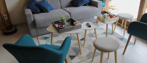 Un salon moderne avec un canapé gris, des coussins bleus, une table basse et des fauteuils turquoise.