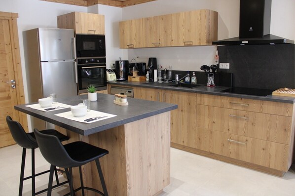A modern kitchen with wooden cabinets, a stainless steel refrigerator, a built-in oven, and a black range hood.