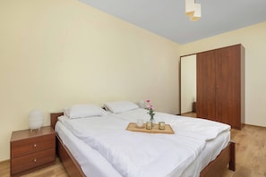 Un letto rifatto con lenzuola bianche, un comodino con una lampada e un armadio in legno.