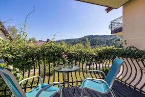 Un balcone con tavolo e sedie, immerso nel verde e vista su una collina boscosa.