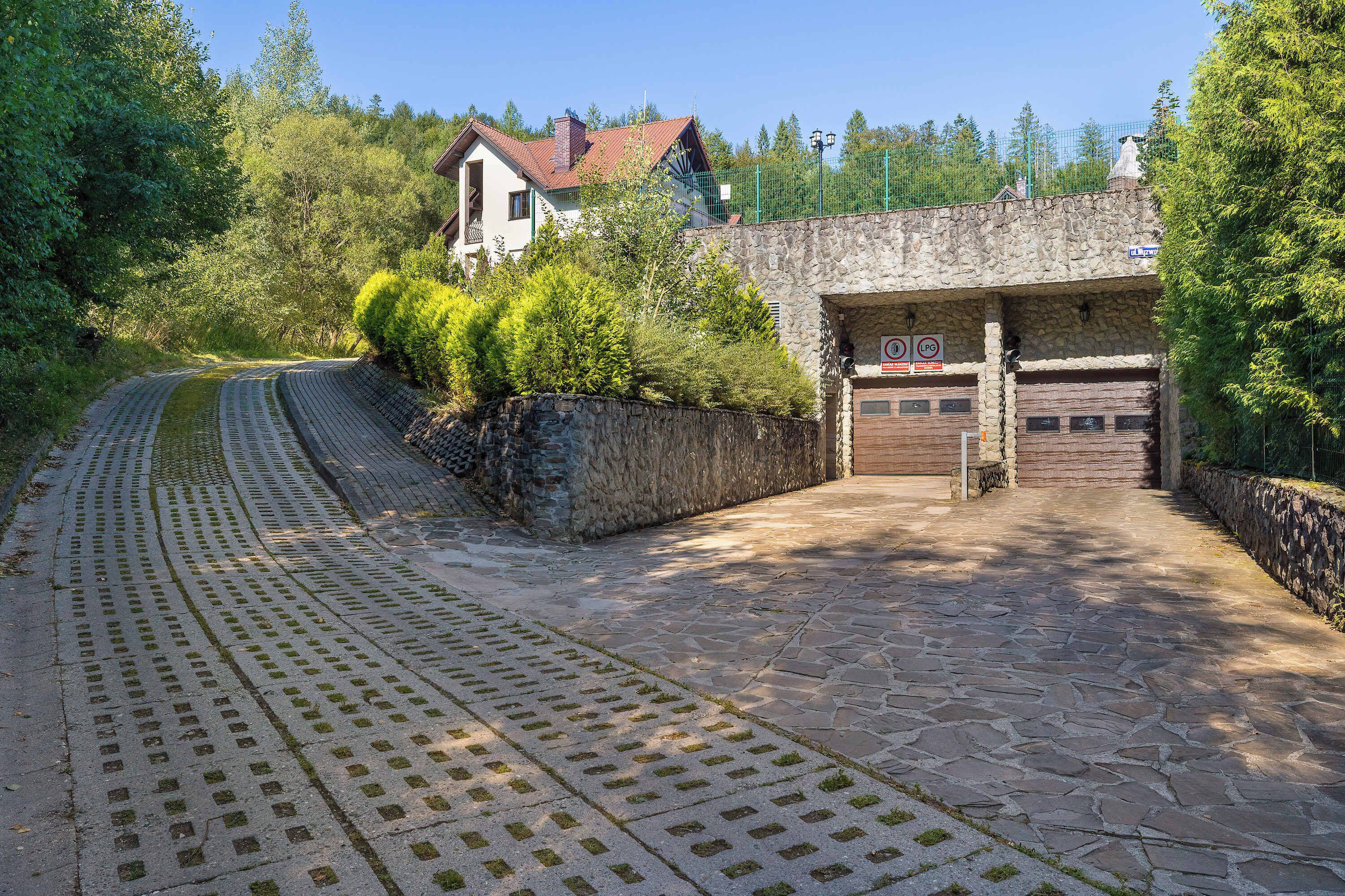 A stone pathway leading to a building with a garage door, surrounded by greenery and trees.