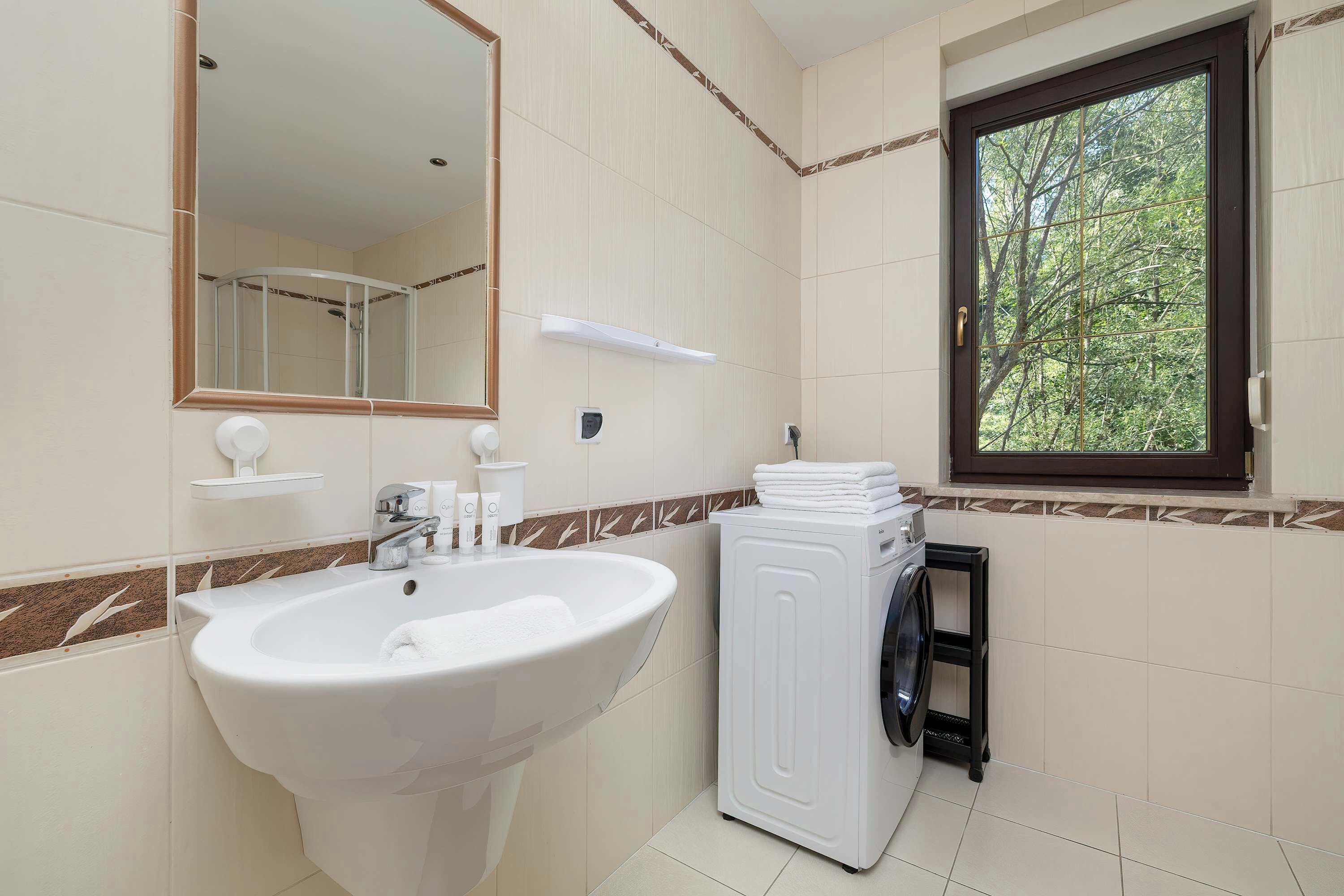 A bathroom with a sink, mirror, window, and a washing machine.