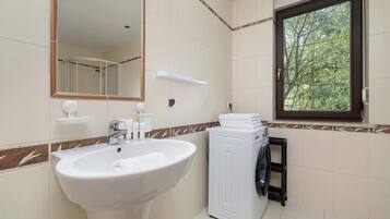 A bathroom with a sink, mirror, window, and a washing machine.