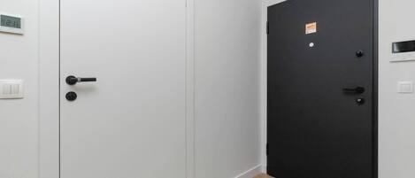 A room with a white door, a black door, and a light switch on the wall.