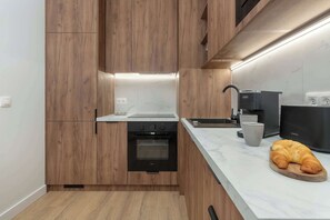 Cuina moderna amb armaris de fusta, forn encastat, rentapelats i taulell de treball amb una barra de pa.