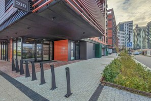 A modern building with a glass facade, a red-brick entrance, and a parking sign. - Comfortable Apartment with a Garden | Parking (Gdańsk)