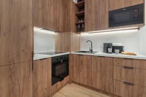 Una cuina moderna amb armaris de fusta, forn integrat, microones i cafetera.