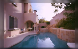 Una piscina con un muro de piedra y un patio con sillas y una mesa.