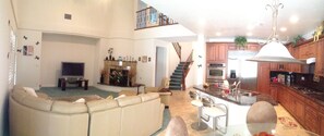A living room with a sofa, a television, and a fireplace. There is a kitchen area with a stove, oven, and bar stools. - Luxury 6BR Summerlin West Oasis Detached Casita Gated Community (Las Vegas)